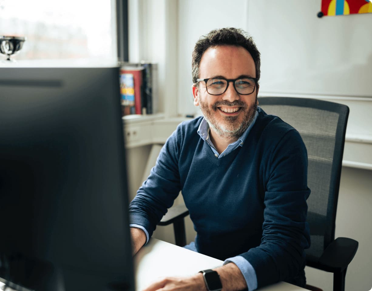 Lächelnder Mann sitzt an einem Schreibtisch mit einem Computer.